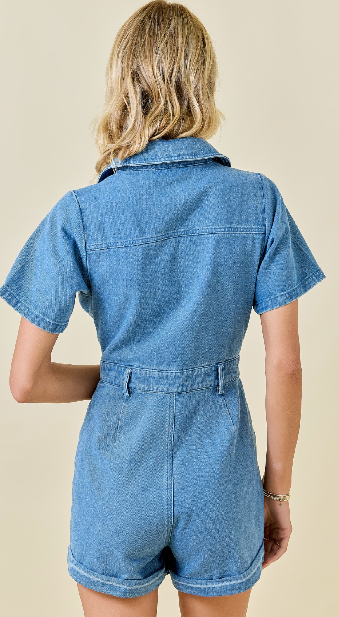 Person wearing a denim romper on a beige background